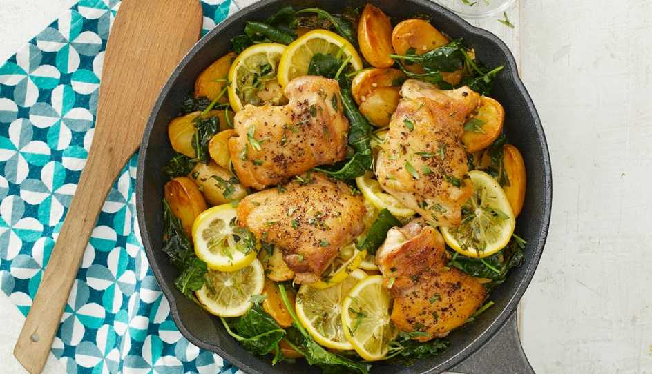 A close-up view of skillet lemon chicken and potatoes with kale in a skillet