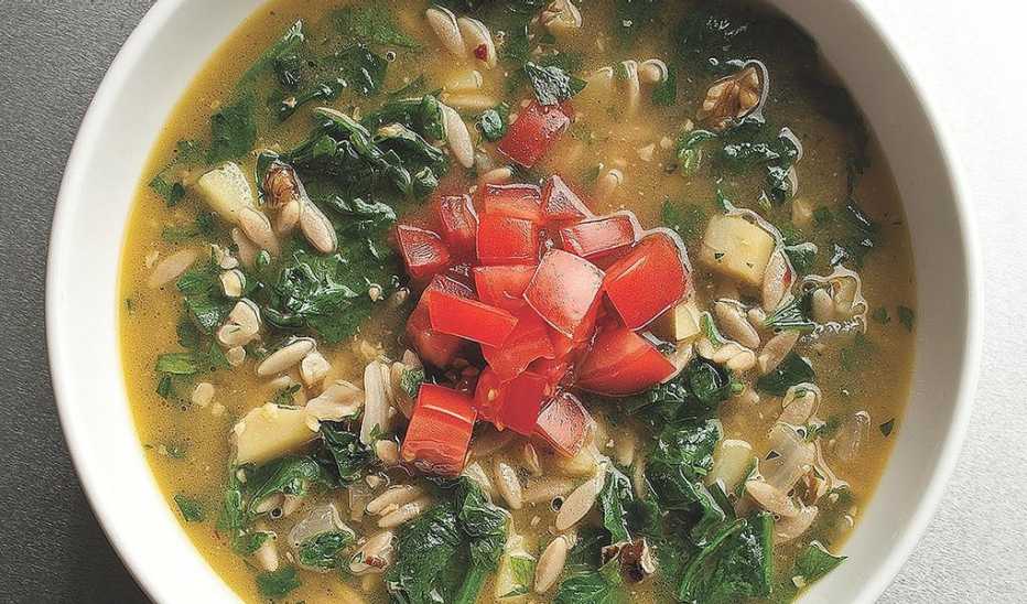A close-up view of rustic parsley and orzo soup with walnuts in a bowl