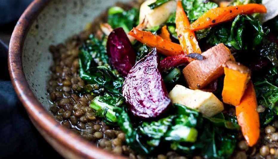 Roasted root veggies and greens over spiced lentils A close-up view of roasted root veggies and greens over spiced lentils in a bowl