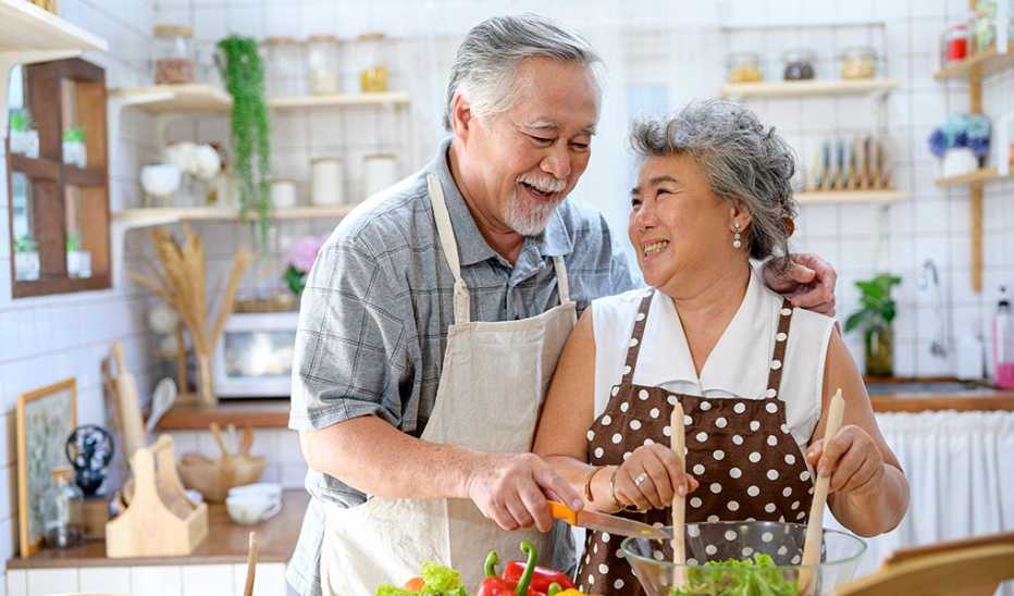 A man and woman smiling and preparing food together at home
