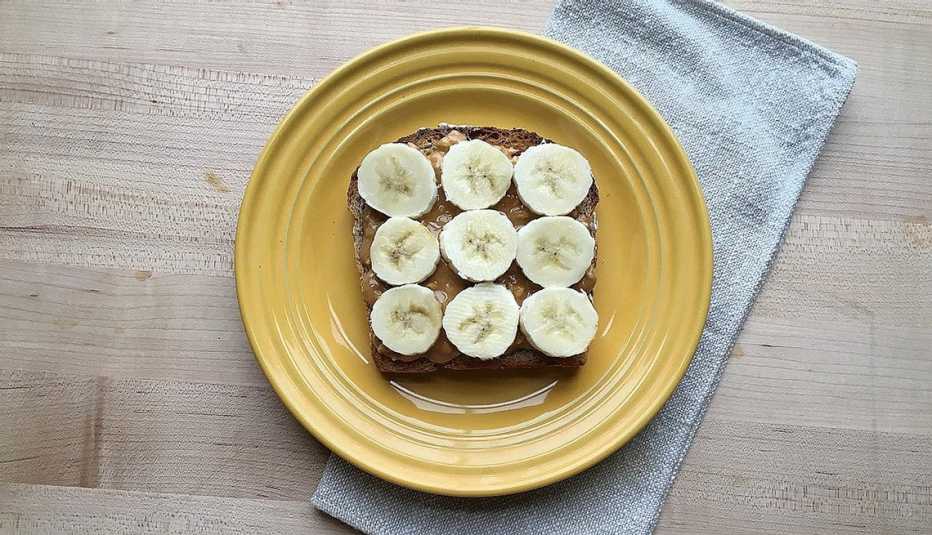 A close-up view of sprouted-grain toast with peanut butter and banana on a plate
