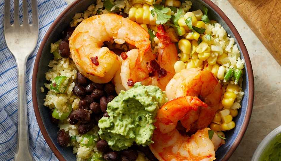 A close-up view of a Southwestern cauliflower rice bowl with shrimp and avocado crema