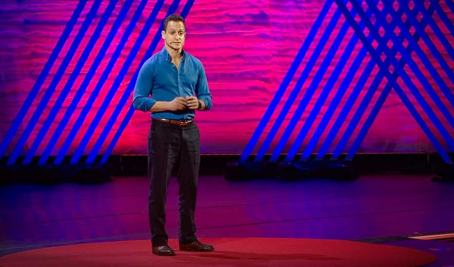 A man, Erez Yoeli, speaking on stage at a TED event