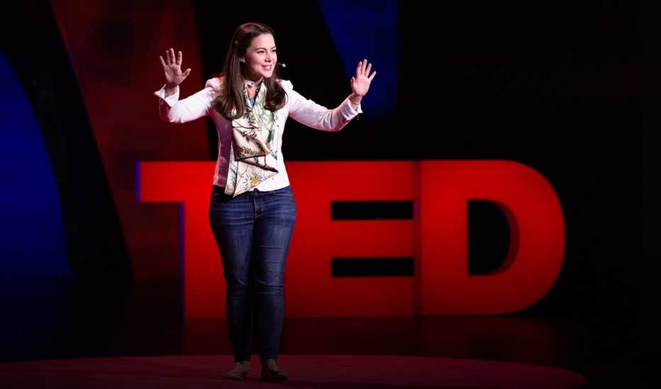A woman, Julia Dhar, speaking on stage at TED event