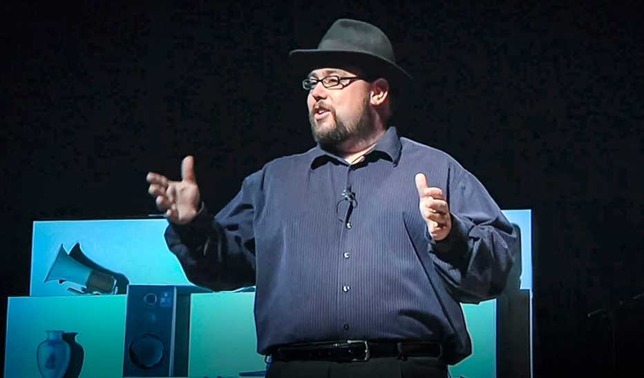 A man, Drew Dudley, speaking on stage at a TED event