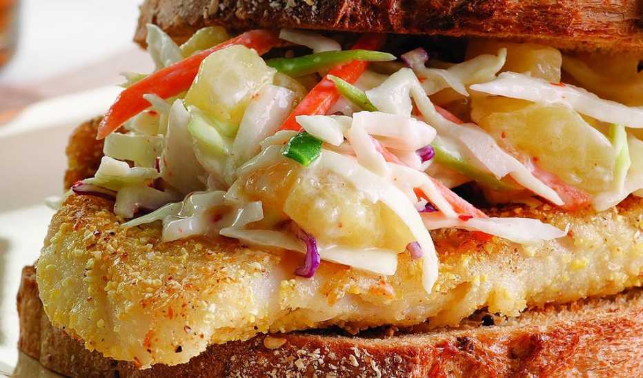 A close-up view of a crispy fish sandwich with pineapple slaw