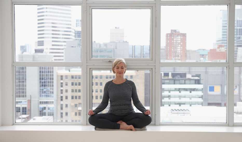 A woman doing yoga in front of a loft window  in an urban city