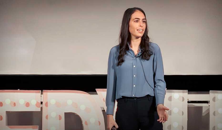 A woman, Fallon Goodman, speaking on stage at a TED event