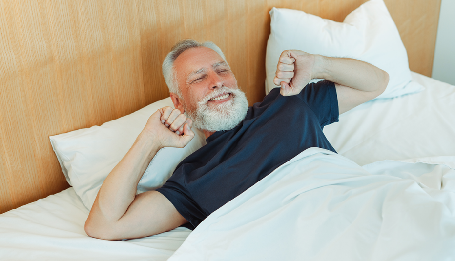 A smiling man stretching his arms as he wakes up in a bed