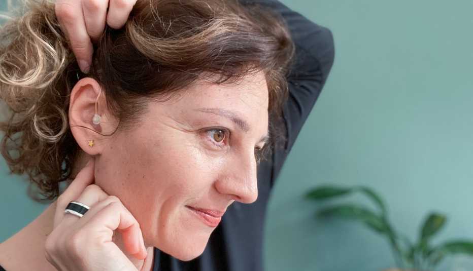 A smiling woman showing her hearing aid in her ear
