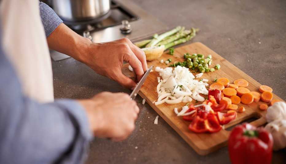 The hands of a person chopping vegetables on a cutting board