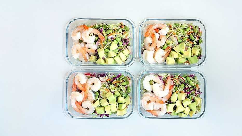 A close-up view of spicy slaw bowls with shrimp and edamame in four containers