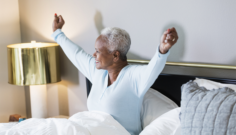 A smiling woman waking up from bed sitting up with her arms stretched