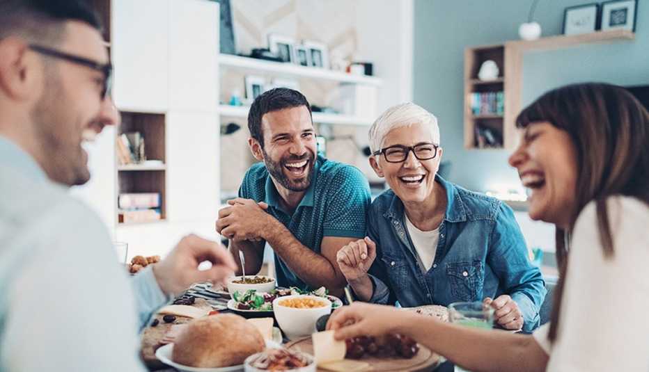 Two men and two women laughing together during a meal at a table in a home