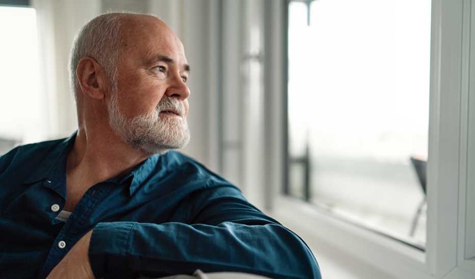 A man sitting on a couch alone and looking out of a window