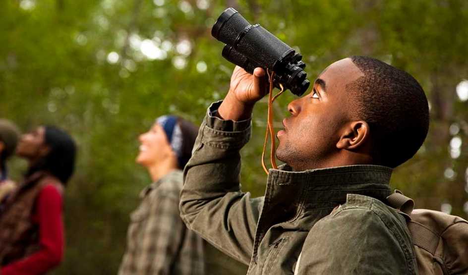 A man using binoculars on a hike with other people