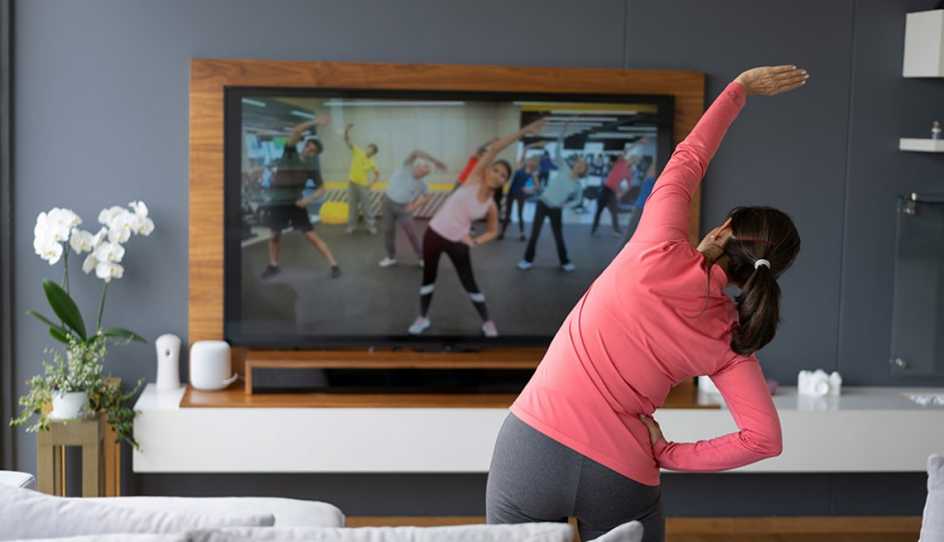 Back view of a woman stretching as she watches an exercise class on TV